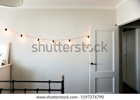 
a garland is burning in a beautiful room with white walls, a door, an iron bed and a corridor
