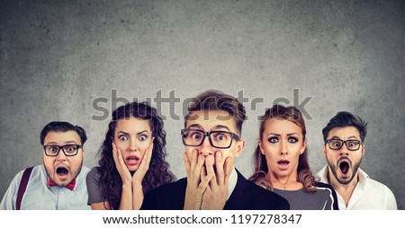 Shocked man in glasses and his scared friends pose against gray wall background. Emotional horrified group people see something unexpected. Human reaction concept Royalty-Free Stock Photo #1197278347