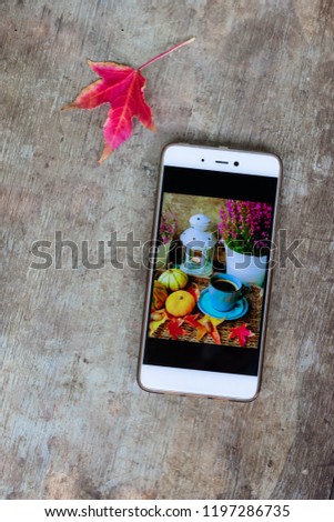 Top view of a mobile phone with an autumn or Halloween decoration screen picture or wallpaper on old rustic wooden background. Phone holiday decoration or images concept