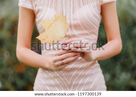 The bride holds an autumn leaf. Maple leaf in the hands of the girl.