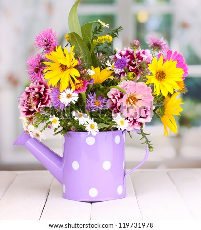 beautiful bouquet of bright flowers in watering can on wooden table