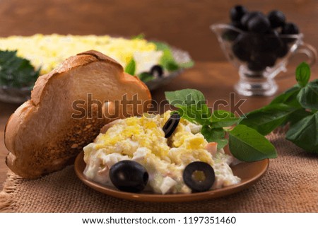 Salad of sliced boiled eggs, crab meat with cheese and cucumber, basil  leaves, chopped marinated black olives, toasted toast.