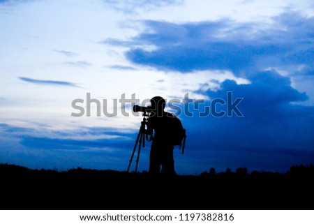 Silhouette of a landscape photographer and tripods in twilight with blurred nature blue sky  background.