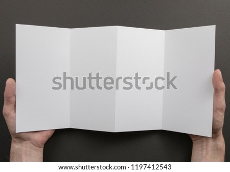 Mens hands holding empty white booklet on gray background. View from above