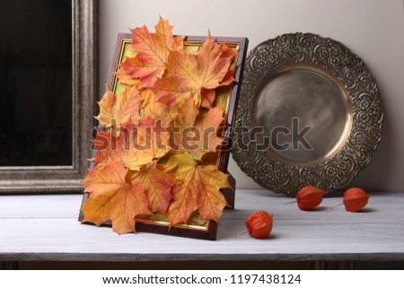 Picture frame  with maple leaves composition as autumn decoration in interior. Handmade colorful natural autumn fall composition in frame and dried plants chinese lantern on wooden shelf.
