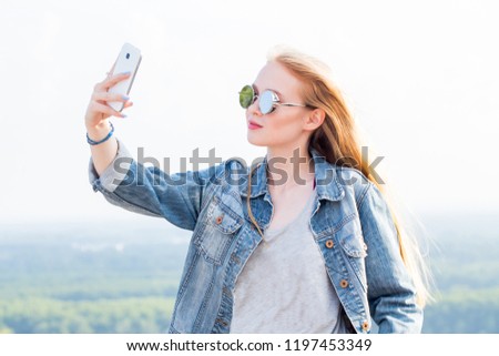 Beautiful young blonde woman in sunglasses takes a selfie against the landscape, nature in the mountains. Modern technology, travel, summer, lifestyle concepts