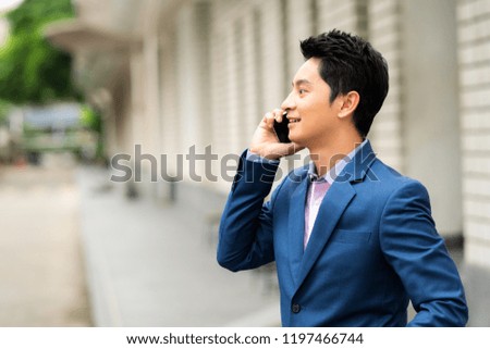 Young Asian businessman talking on a phone on urban background.