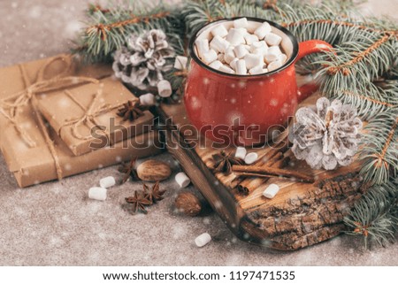 Red cup of hot cocoa with marshmallow on the wooden cutting board with Christmas decorations and snow effect. Horizontal view. Copy space