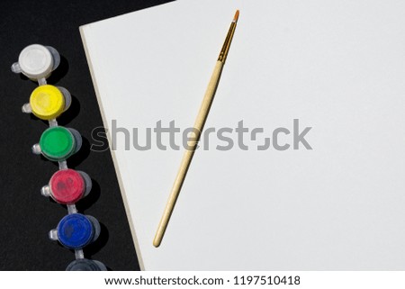 Photo of a piece of drawing paper with a brush next to paint on a black background. View from above