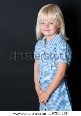 A beautiful little girl poses for school uniform pictures on a black background