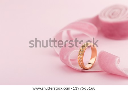Pink gold wedding ring with diamonds and wave pattern on pink background with ribbon. Product concept for jeweler