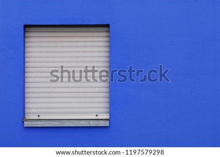 Window with closed gray roller blinds in a blue wall