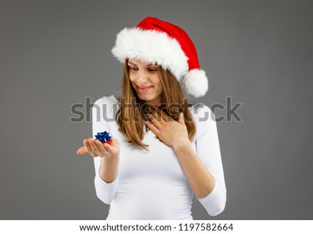 Beautiful woman in Santa Claus clothes holding gift boxes on gray background