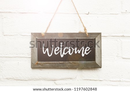 Wooden blackboard with text hello welcome home sign board against white brick wall in sunlight