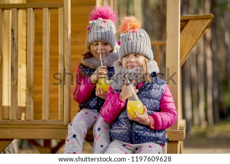 two little girls in a cap and jacket are drinking lemonade in a house in an autumn forest