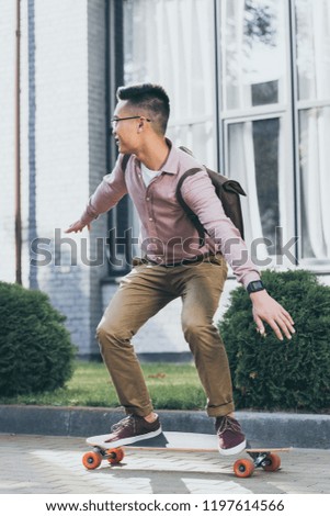 young asian man with backpack riding longboard on street