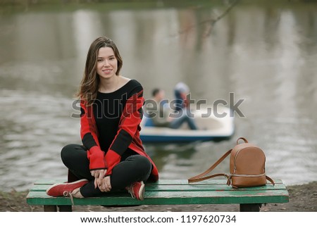 girl is sitting on a garden bench / beautiful model posing sitting in  coat on  bench in  city park, beautiful girl