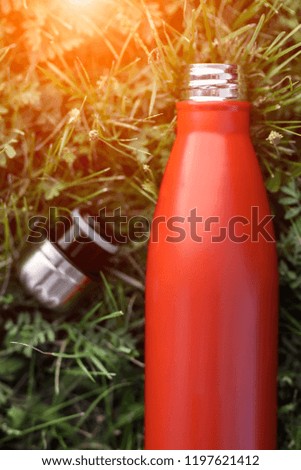 Stainless thermos water bottle, red color. Isolated on green grass background with sunlight effect.