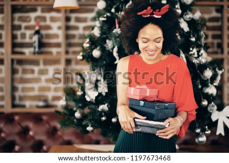 Happy mixed race woman holding gifts and standing in frront of Christmas tree. Christmas holidays concept.