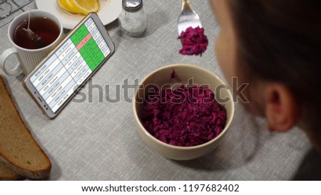 Businesswoman having lunch. On the table is a salad, bread, lemon and tea. She watches online currency quotes on the smartphone screen.