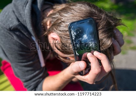 Broken and damaged smartphone with cracks on glass, screen. Young man is disappointed and sad, holding phone in hands. Concept of anger, rage and accident. 
