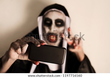 closeup of a frightening evil nun, wearing a typical black and white habit, taking a selfie with a smartphone while giving a V sign