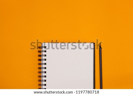 Empty spiral notebook with white page and wooden pencil on orange background. Workplace with notepad on colored background. Sketch-book for input the text, top view.