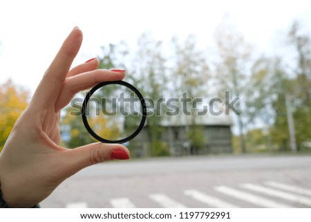 Protective lens on the lens in hand against the background of the autumn landscape and pedestrian crossing horizontal shot