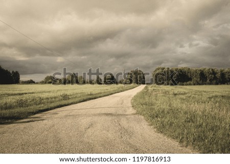 simple country gravel road in summer at countryside with trees around and clouds in the sky - vintage retro look