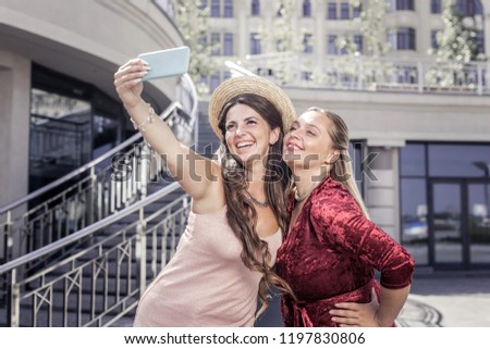 Selfie time. Joyful happy woman holding her smartphone while taking a photo with her sister