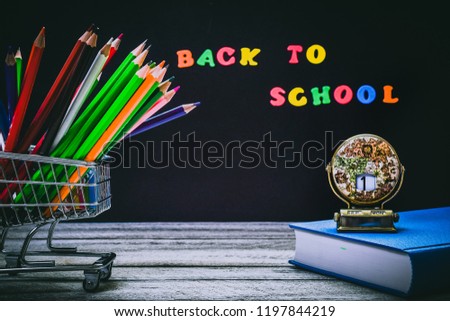 Back to School and Education concept. shopping cart with color pencils and book antique globe calendar with the 1st of September on chalkboard background. school border with copy space