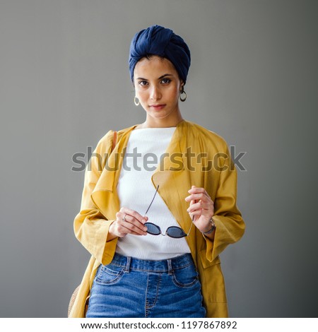 A studio portrait of a young Malay Muslim woman. She is fashionably dressed and is a fan of modest fashion -- she is wearing a turban (hijab head scarf) along with her trendy attire. Royalty-Free Stock Photo #1197867892