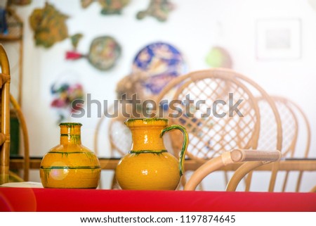 Decorative clay pots, bowls and vases standing on shelf in kitchen. Abstract paintings and colorful drawings on wall in the background. Bright sunlight from corner. Cozy home and atmosphere
