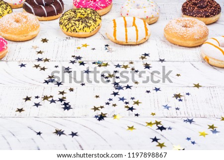 Rows of colorful donuts with sprinkles and different fillings on white background with confetti and streamers