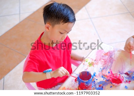 Cute Asian boy painting picture on the cup  at table indoors