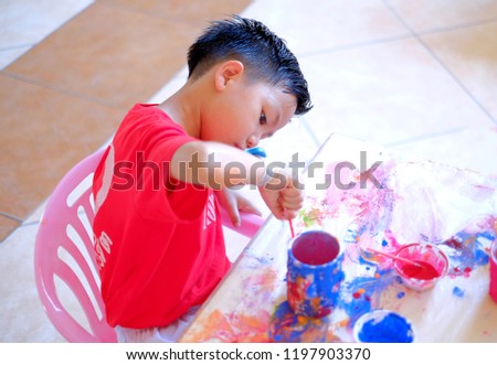 Cute Asian boy painting picture on the cup  at table indoors
