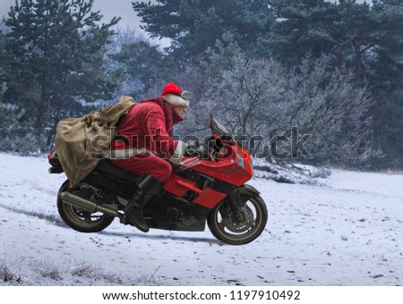 Santa Claus on a red motorcycle with a sack of gifts, drives fast along snow-covered field. Royalty-Free Stock Photo #1197910492