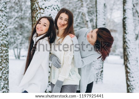 three young and active girls in glowes and scarves stroll through the winter snow covered park