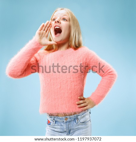 Do not miss. Young casual teen girl shouting. Shout. Crying emotional teenager screaming on blue studio background. Female half-length portrait. Human emotions, facial expression concept. Trendy