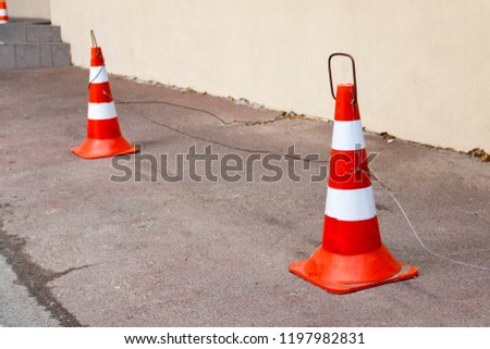 Traffic cone with orange and white stripes on the road in parking, used for road safety. road traffic cones standing on street on gray asphalt during road construction works
