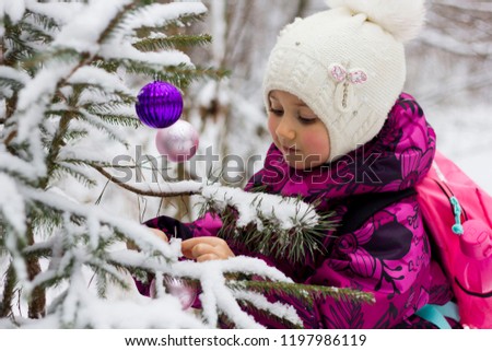 happy girl decorates the tree in the forest with balls and tinsel