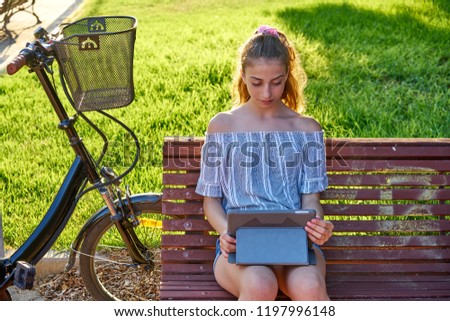 Girl sitting on park bench playing with tablet pc and bike