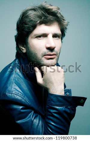 Portrait of a fashionable handsome man in blue jacket over light blue background holding his head. Studio shot