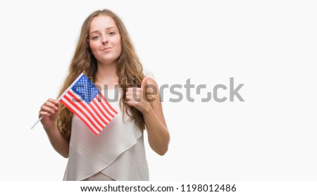 Young blonde woman holding flag of USA happy with big smile doing ok sign, thumb up with fingers, excellent sign