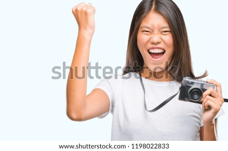 Young asian woman holding vintagera photo camera over isolated background annoyed and frustrated shouting with anger, crazy and yelling with raised hand, anger concept