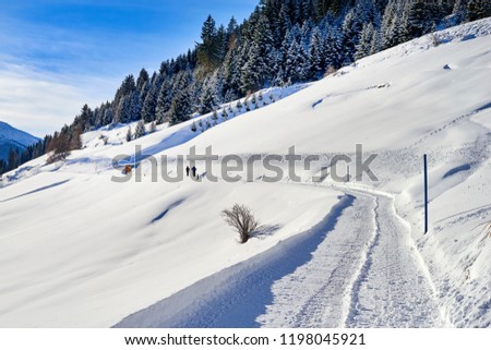 Tyrol Alps winter landscape: snow-covered countryside road on hill slope, two people are walking