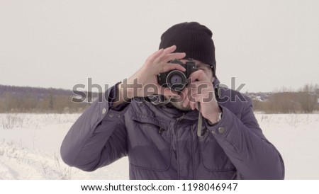 A man takes a picture. shoots on an old camera. Winter season. Warm clothing. Snow field. Bright day. Largest species. 4K video