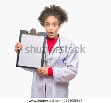 Young afro american doctor woman holding clipboard over isolated background scared in shock with a surprise face, afraid and excited with fear expression