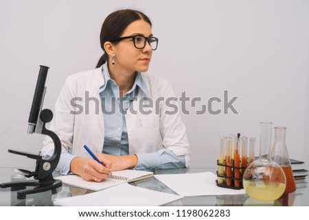 Beautiful medical doctors in gloves and glasses are working with substances in test tubes and microscope at the lab. Photo of attractive concentrated female doctor writing prescription on special form