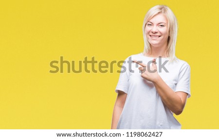 Young beautiful blonde woman wearing white t-shirt over isolated background cheerful with a smile of face pointing with hand and finger up to the side with happy and natural expression on face